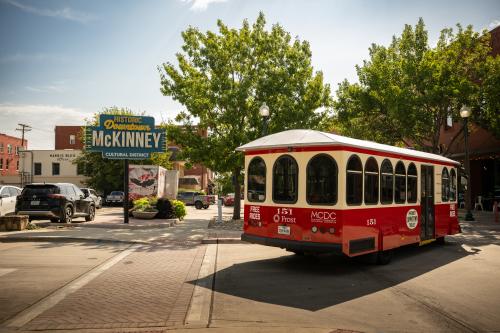 Red and white Downtown McKinney trolley driving past the neon Historic Downtown McKinney sign.