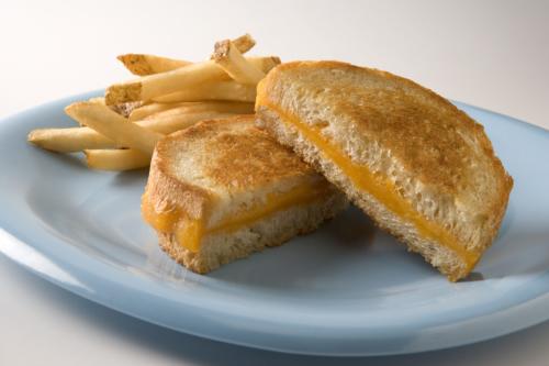 A grilled cheese sandwich cut in half with melted cheese on a blue plate, accompanied by a side of golden French fries.
