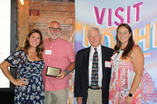 Four smiling men and women stand in front of colorful backdrop, one person is holding an award.