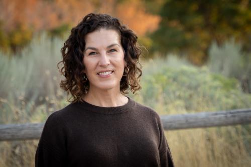 Smiling woman in a black shirt in front of a natural fence and sage brush