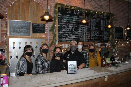 A group poses in front of the bar at Fall Street Brewing with their November 2020 business of the month plaque