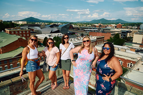 5 women on a rooftop bar with city in the background
