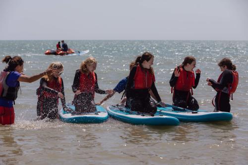 A group of young people wearing red life vests sit on paddleboards in the sea at Eastbourne