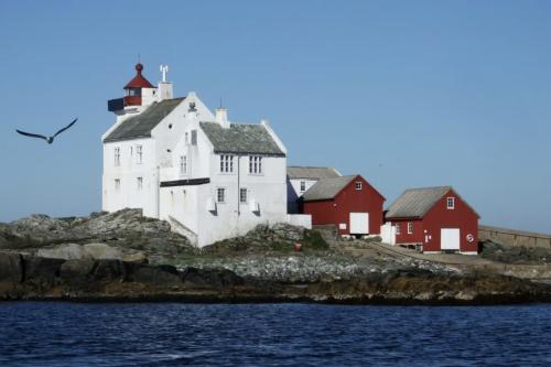 Et fyr i bakgrunnen, men røde og hvite hus foran. Vann helt i forgrunnen.