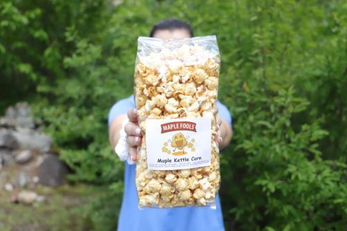 A man holds up a bag of Maple Fools Kettle Corn