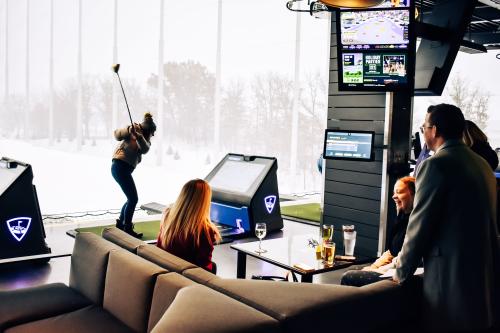 Group at Topgolf with friends enjoying a conversation while a golfer swings at a ball.