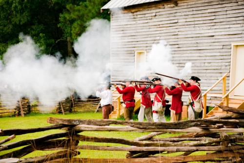 A live reenactment of a war with a wooden building in the background