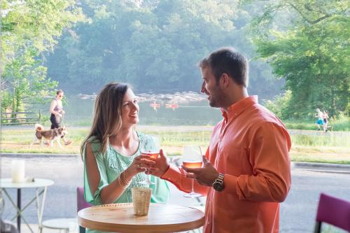 A man and a woman sharing wine together with a lake and a person walking their dog in the background