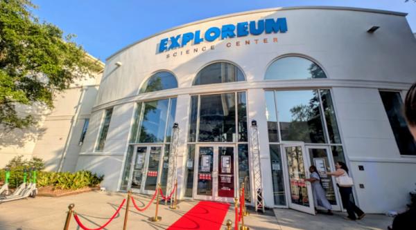 The Exploreum Science Center is a tall white building with tall arched windows and glass doors