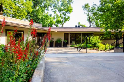 A modern building surrounded by lush greenery and vibrant red flowers, featuring a smooth pathway and accessible steps leading to the entrance.