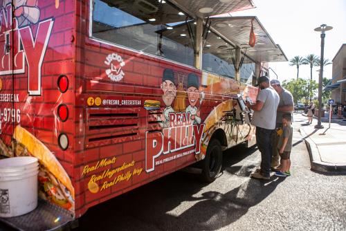 Two men and young boy stand in front of food truck ordering food on tablet