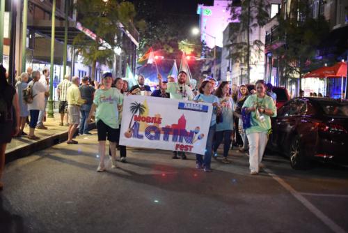 An image of people walking down the street carrying a "Mobile Latin Fest" banner