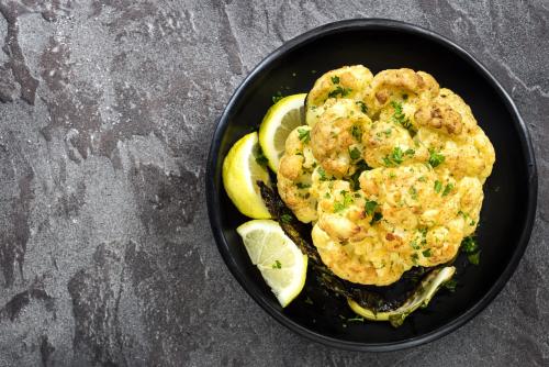 Roasted whole cauliflower with lemon, in black serving dish, top view.