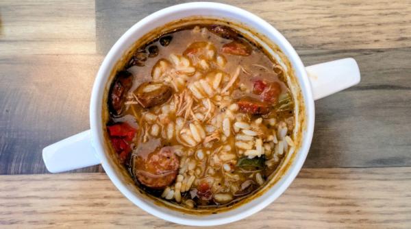 A photo taken overhead of a bowl of gumbo, with sausage, rice and herbs