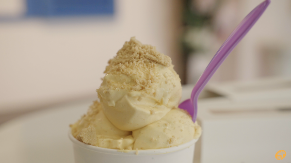 Image of a double scoop of pumpkin spice ice cream placed in a white cup with a pink spoon.