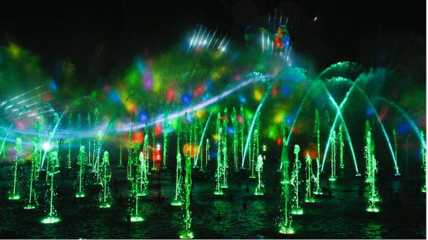 Image of World of Color at Disney California Adventure. Image shows water fountains, colored green, seemingly dancing in the air. Projections are displayed on the mist produced by the water fountains.