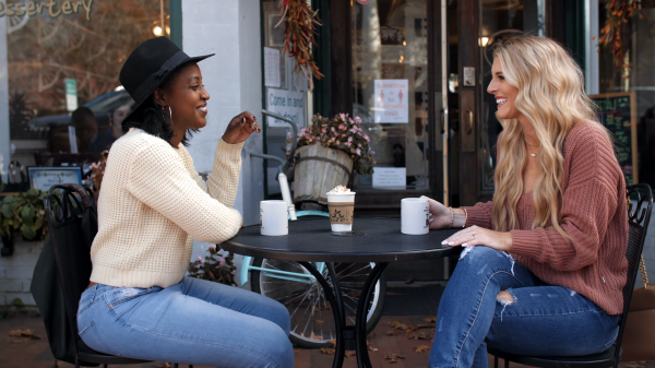 Two girls having coffee outside a shop, Fall leaves on the ground, girls are dressed in fall sweaters