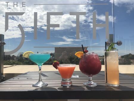Four cocktails lined up against a sign that reads The FIFTH.