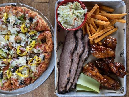Pizza, Brisket, Fries, Celery, Wings, and Coleslaw all on a platter on the table.