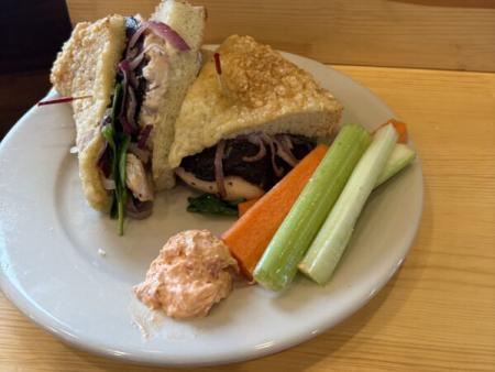 Sandwich with Parmesan Focaccia Bread, portabella mushrooms, roasted red onion, whole grilled chicken breast and parmesan spread topped with lightly dressed fresh spinach on a plate.