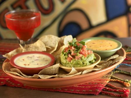 A basket of chips, queso, and guacamole in the foreground and a red margarita in the background from Margaritas in Green Bay, Wisconsin
