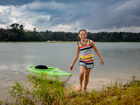 A young girl pulls in a green kayak from the lake that surround Howell Woods.