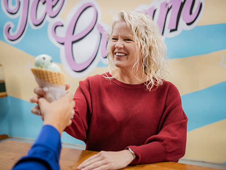 A woman smiles as she accepts an ice cream cone filled with mint-chocolate chi[p ice cream at Old Fashioned Ice Cream.