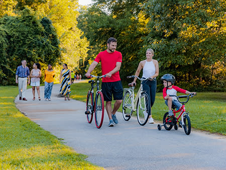 A little boy rides a bicycle while his parents walk their bikes behind him along the Buffalo Greenway in Smithfield, NC.