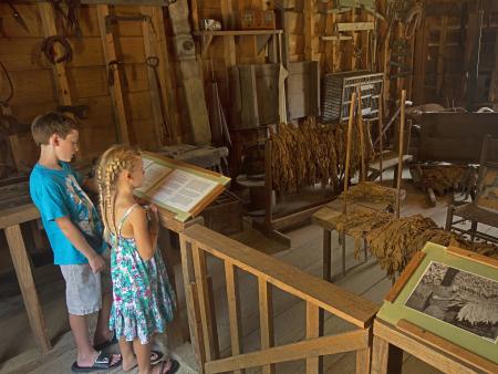 Two children stand at an interactive barn exhibit to read the information on the plaque at the Tobacco Farm Life Museum in Kenly, NC