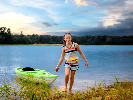 A young girl pulls in a green kayak from the lake that surround Howell Woods.