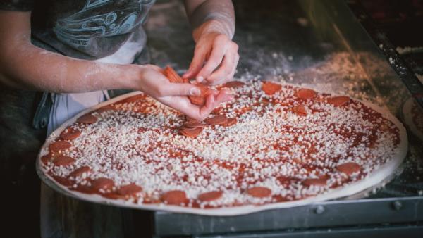 Pizza chef at Little Wing Pizzeria putting pepperoni onto a 24 inch pizza