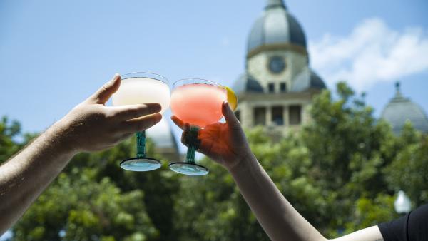 Two people cheers glasses of margaritas with the courthouse in the background