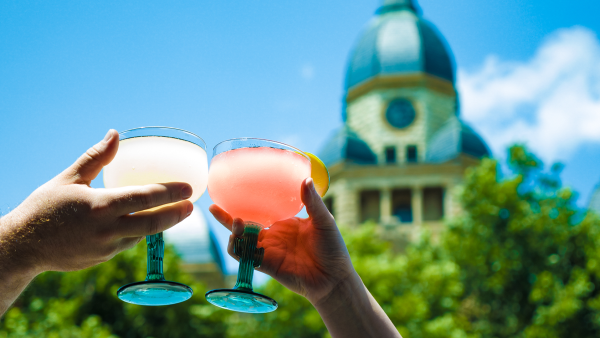 Two people cheers glasses of margaritas with the courthouse in the background