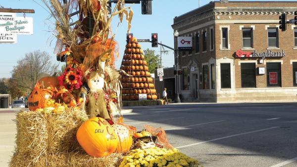 A display of fall hay bales, pumpkins and scarecrows sits in the foreground with the 17-foot tall Pumpkin Tree in downtown Wakarusa in the background