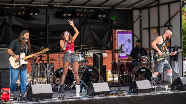 A frontwoman throws her arms into the air as she sings accompanied by a band at the Steel Horse Rally