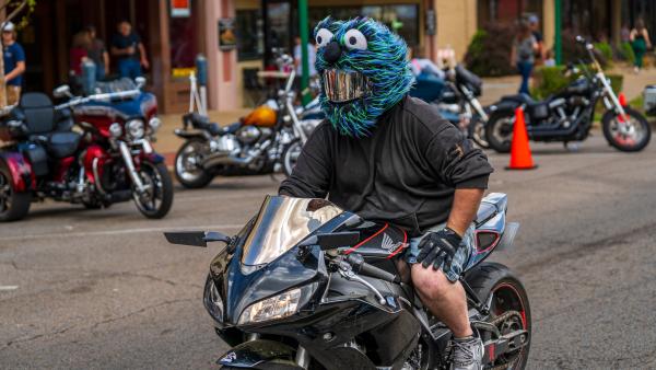 A man rides through the Steel Horse Rally with a furry, cartoonish, muppet-like, helmet.