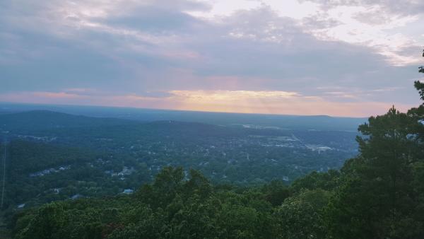 Scenic overlook from Blevins Gap Nature Preserve with wooded hills and Huntsville below beneath a cloudy sunset sky.
