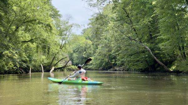 Person kayaking down the calm Flint River surrounded by lush green trees and peaceful wooded scenery near Huntsville, Alabama.