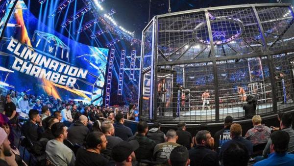 The cage that wrestlers fight in surrounded by the crowd.