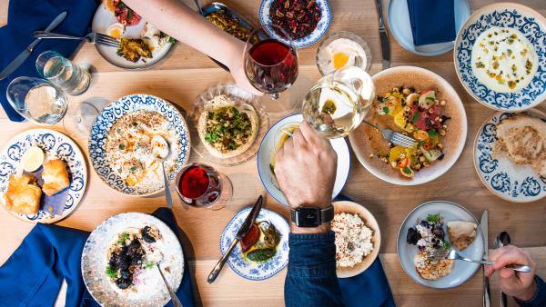 Overhead spread of food with two hands mid-toast with wine glasses