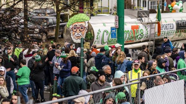 A tank full of green beer with a giant picture of a man's face on the back surrounded by a crowd