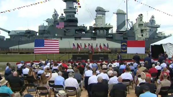 Podium and crowd with flags in front of World War II Monument in Wilmington, NC