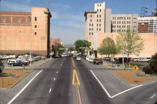 Description An area near First Street and Central Avenue in downtown Albuquerque, New Mexico. From the point of view of the camera, a paved road stretches ahead and into the background of the image and another road curves to the right side of the frame. On the left side of the road, the Sunshine Building and its parking lot can be seen.