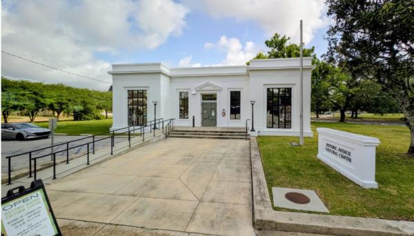 The Historic Avenue Cultural Center is a white block building with large windows and double wooden doors