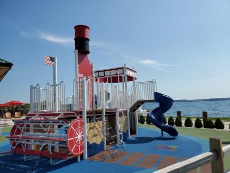 jungle gym that replicates a steamboat with paddle and slide next to lake