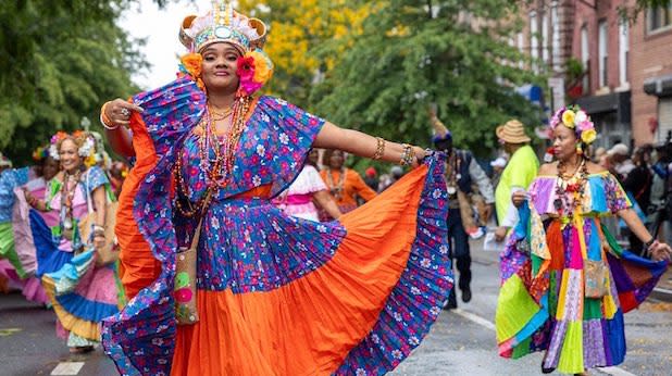 A woman dress in a brightly-colored blue and orange traditional dress and crown dances in the Panamanian Day Parade