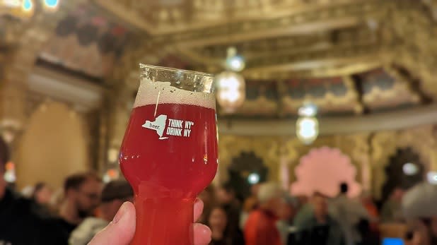 A person holds up a glass with the words "Think NY Drink NY" at the Landmark Theatre in Syracuse during the New York State Craft Brewers Festival