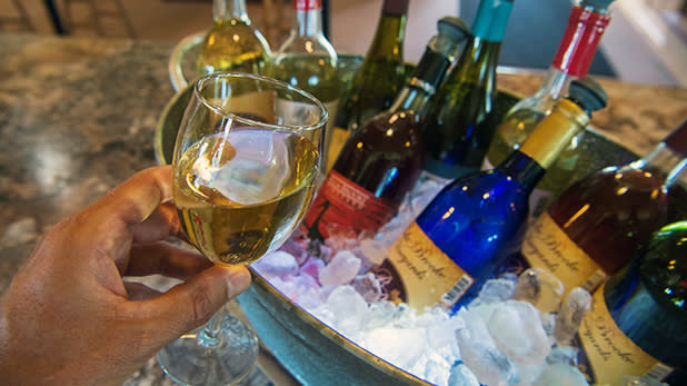 A man holds a glass a white wine next to an ice bucket stacked with wine bottles