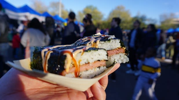 A close up of musubi with a gathering crowd in the background at the Queens Night Market
