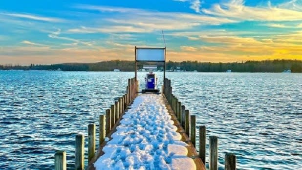 View looking out at a blue gas pump on the end of a narrow dock covered in snow on Chautauqua Lake at sunset